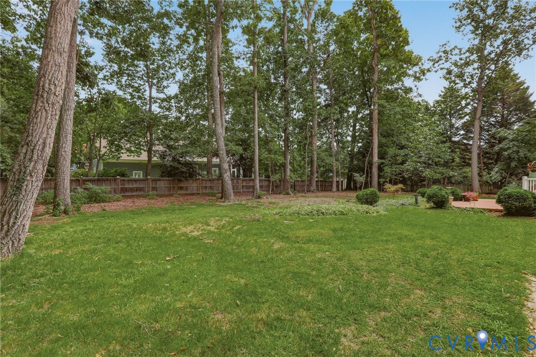 Expansive backyard featuring a lush grass lawn, mature trees, wood privacy fencing, and a brick patio