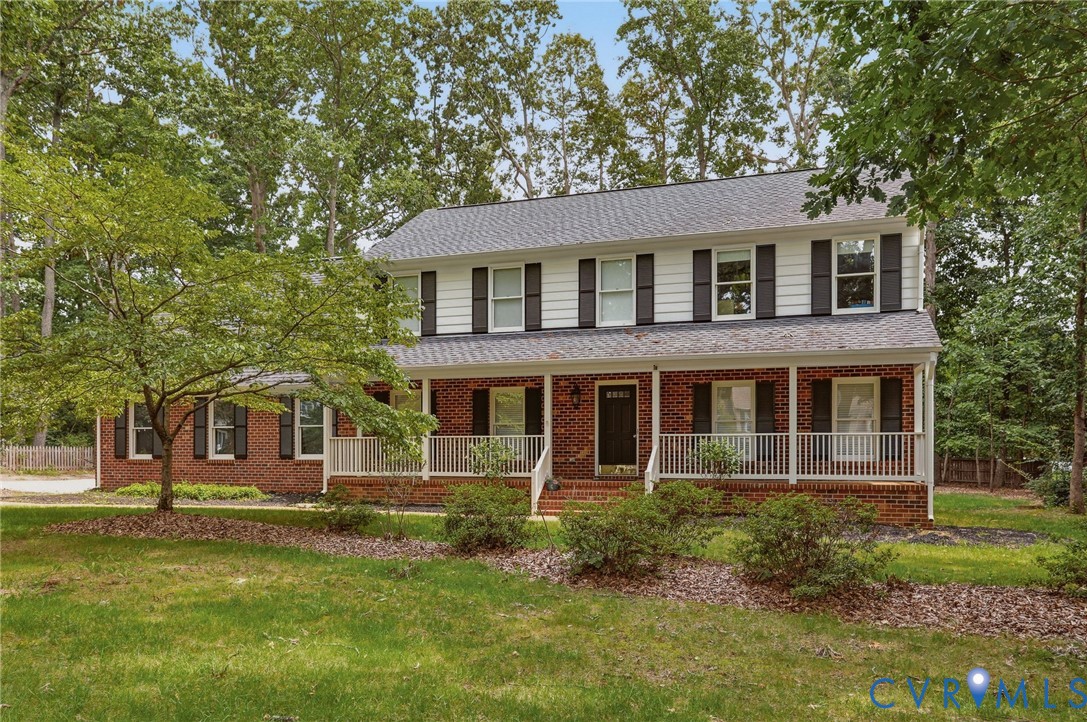 Two-story colonial exterior featuring red brick lower siding, white horizontal upper siding, dark shutters, and a full-length covered front porch with white railing