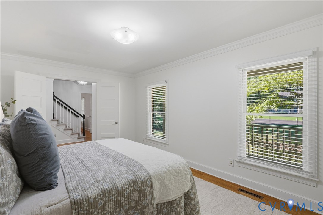 Room featuring crown molding, neutral wall finishes, wood-finish flooring, and multiple windows with horizontal blinds
