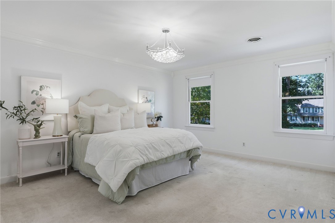 Room featuring neutral wall-to-wall carpeting, crown molding, double-hung windows, and a decorative crystal-style chandelier
