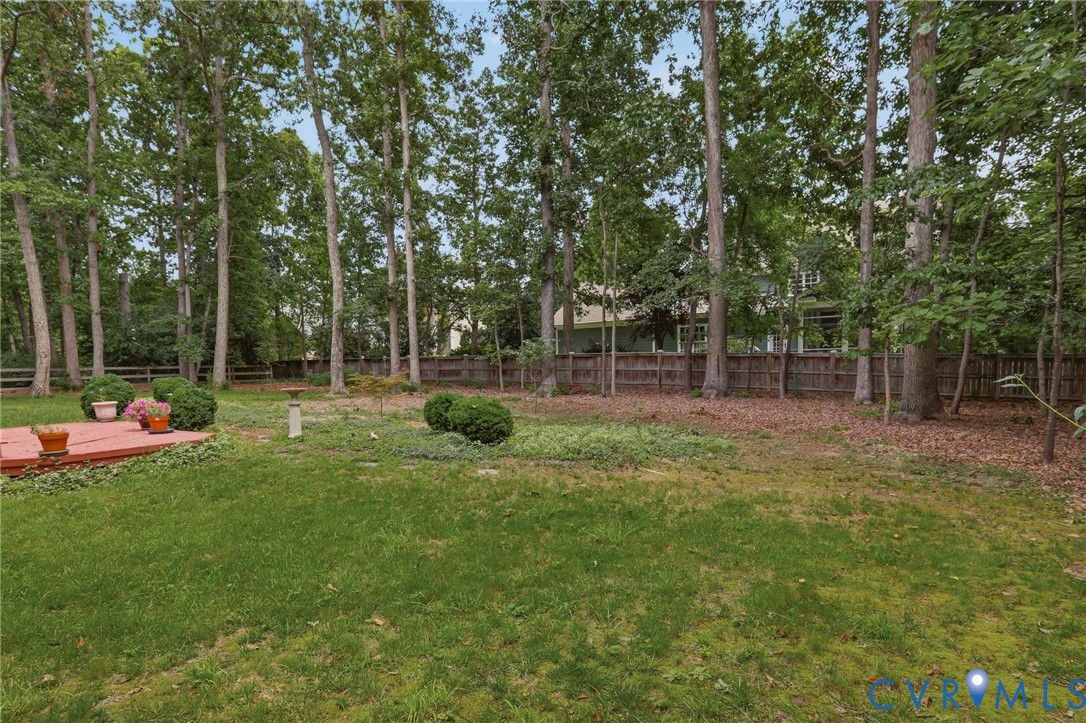 Backyard featuring a wood deck, perimeter wood fencing, manicured shrubbery, and mature trees