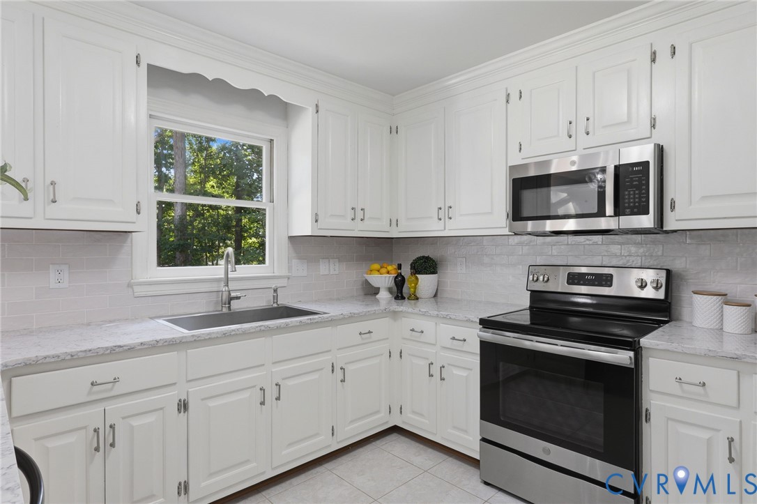 Kitchen featuring white shaker-style cabinetry, stone-finish countertops, subway tile backsplash, stainless steel appliances, and an undermount sink