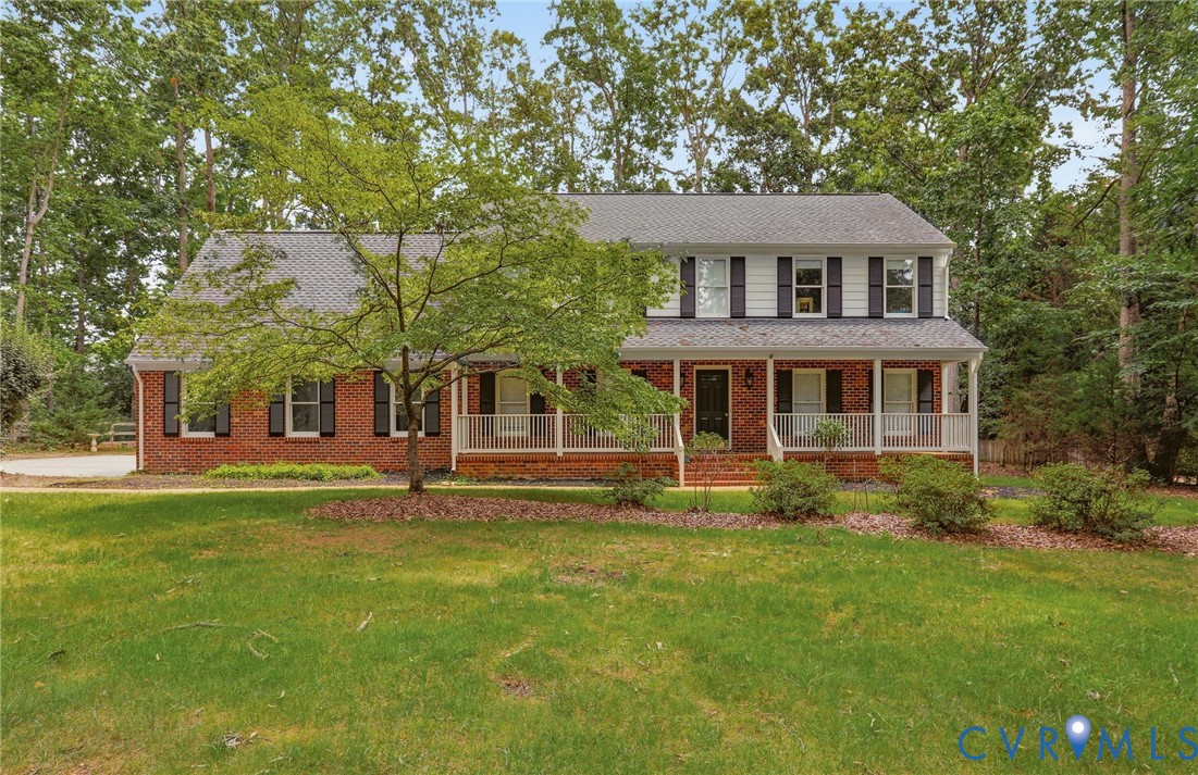 Traditional two-story exterior featuring a brick facade, white siding, a covered front porch with a wood-finish floor, shuttered windows, and a shingled roof Traditional two-story exterior featuring a brick facade, white siding, a covered front porch with a wood-finish floor, shuttered windows, and a shingled roof