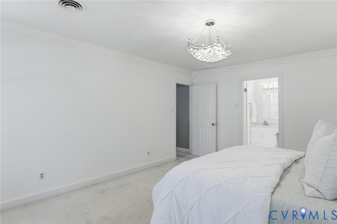 Room featuring crown molding, neutral carpeting, and a multi-tiered crystal chandelier