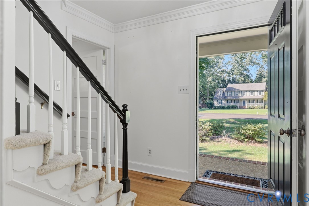 Foyer featuring wood-finish flooring, a staircase with a contrasting dark railing and white balusters, and a paneled entry door with transom detailing Foyer featuring wood-finish flooring, a staircase with a contrasting dark railing and white balusters, and a paneled entry door with transom detailing