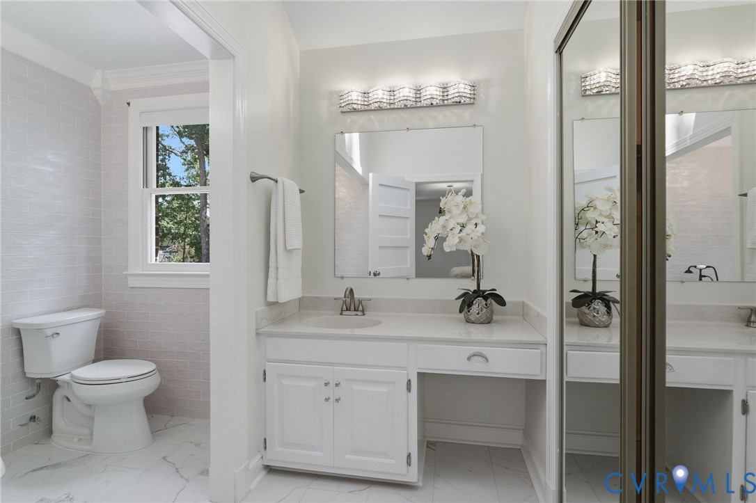 Bathroom featuring a vanity with integrated cabinetry, solid-surface countertop, rectangular mirror, multi-bulb wall lighting, and large-format tile flooring