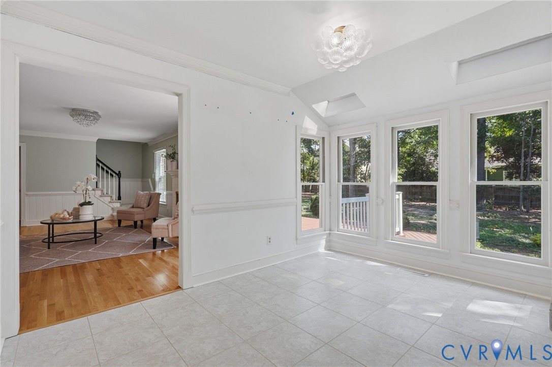 Sunroom featuring large windows, vaulted ceiling, skylights, tile flooring, and decorative flush-mount lighting