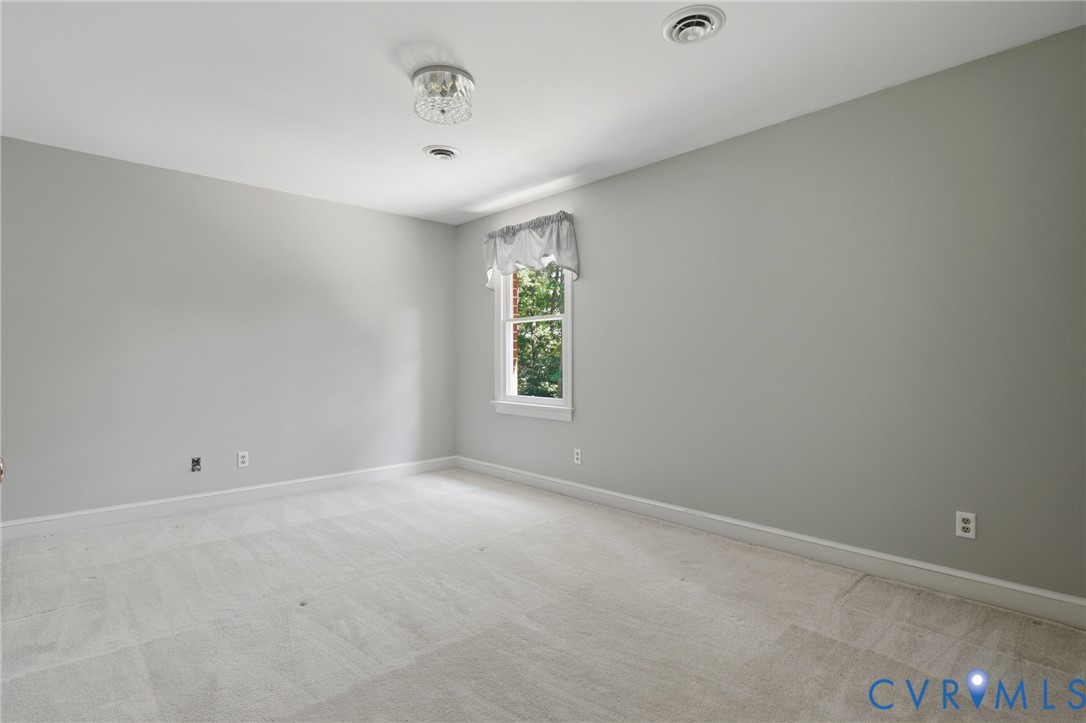 Neutral-toned interior space featuring wall-to-wall carpeting, a single-pane window, and a decorative flush-mount ceiling light fixture