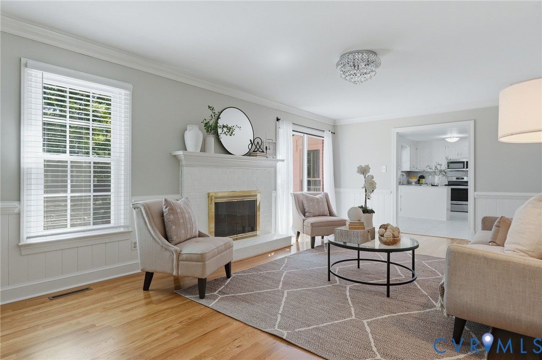 Living room featuring wood-finish flooring, white wainscoting, crown molding, and a fireplace with a mantel