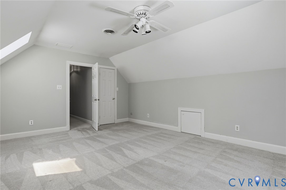 Sloped ceilings featuring a skylight, wall-to-wall carpeting, ceiling fan with attached lighting, and built-in knee-wall storage access
