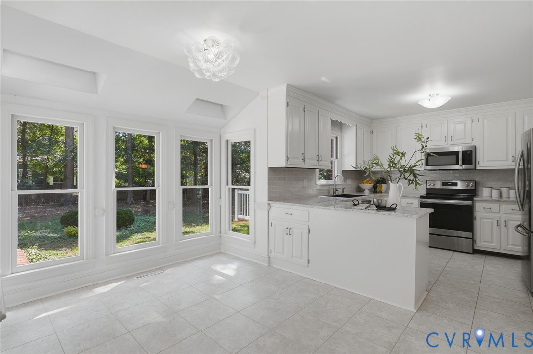 Kitchen featuring white cabinetry, light-toned stone-finish countertops, stainless steel appliances, large-format tile flooring, and multiple floor-to-ceiling windows