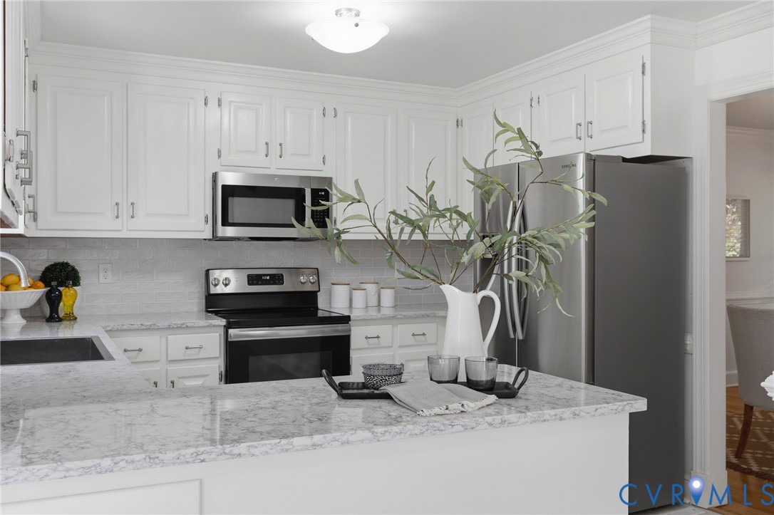 Kitchen featuring white cabinetry, stone-finish countertops, stainless steel appliances, and a central peninsula