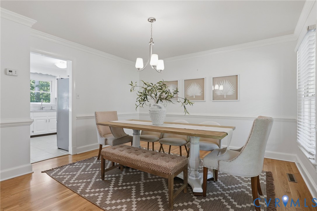 Dining area featuring wood-finish flooring, white chair rail molding, crown molding, and a three-light metal chandelier