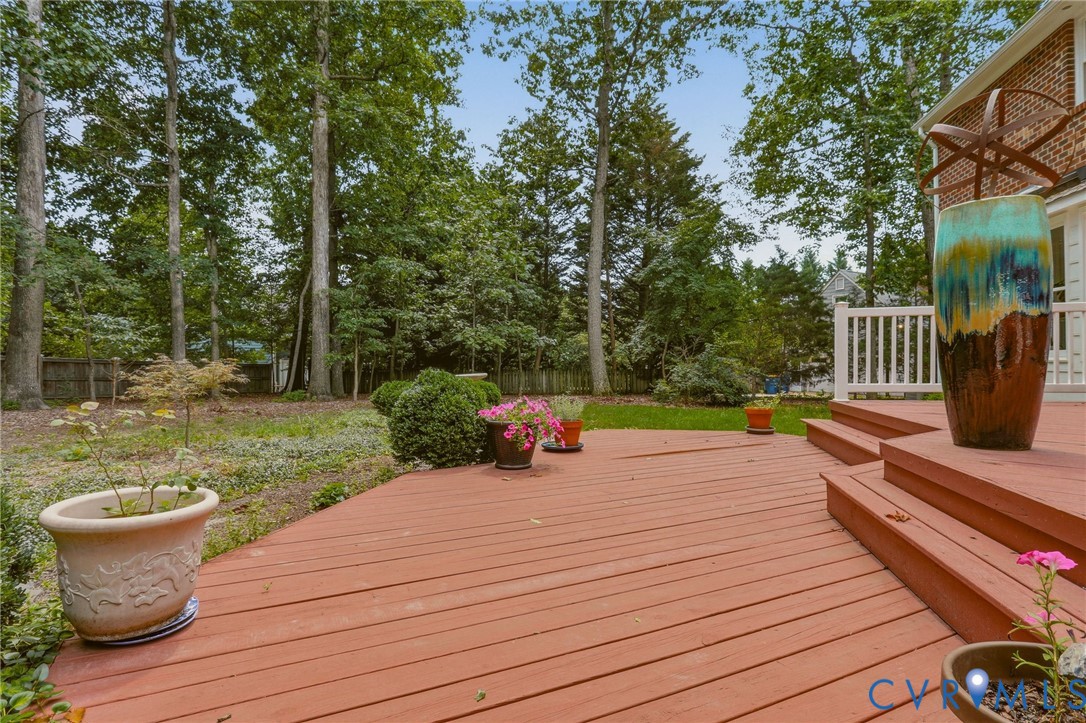 Multi-level wood deck featuring white balustrades and an expansive backyard with mature trees and professional landscaping