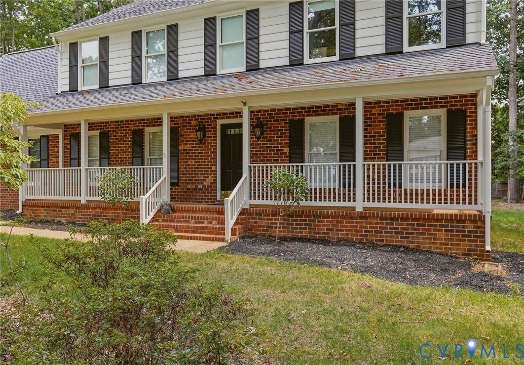 Two-story exterior featuring a brick facade, white horizontal siding, dark decorative shutters, a shingled roof, and a covered front porch with white railing Two-story exterior featuring a brick facade, white horizontal siding, dark decorative shutters, a shingled roof, and a covered front porch with white railing