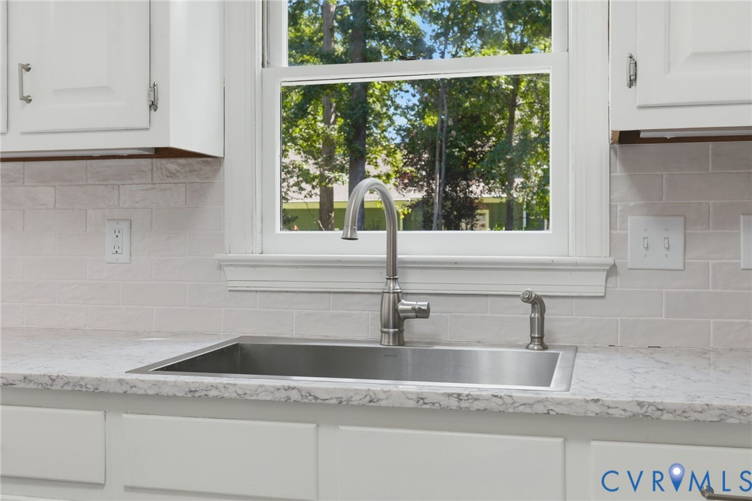 Kitchen featuring white shaker-style cabinetry, a stone-patterned countertop, a stainless steel undermount sink with a high-arch gooseneck faucet, and a light-toned brick-style backsplash