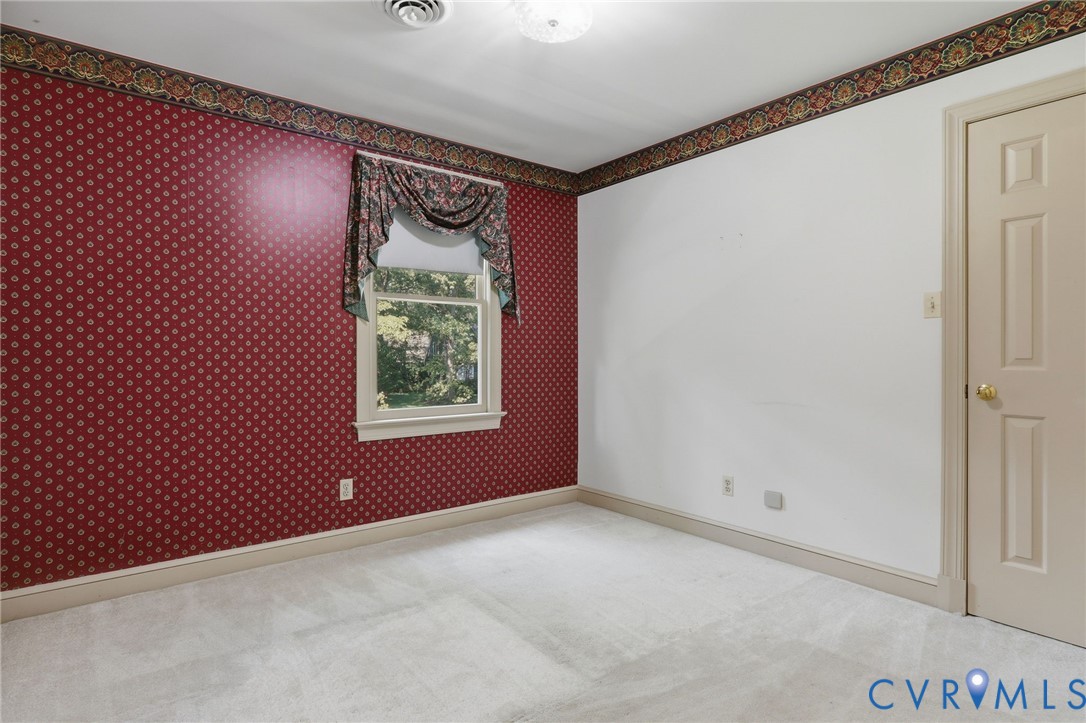 Neutral carpeting, patterned wallpaper, and a single-hung window with a decorative valance