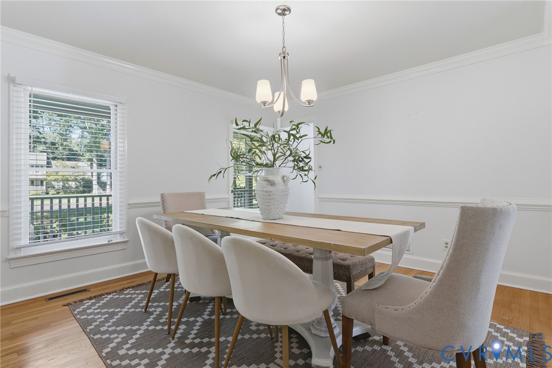 Dining area featuring hardwood flooring, crown molding, chair rail trim, and a three-light brushed nickel chandelier
