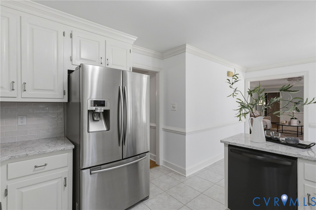 Kitchen featuring white shaker-style cabinetry, stone-finish countertops, subway tile backsplash, stainless steel refrigerator, and ceramic tile flooring