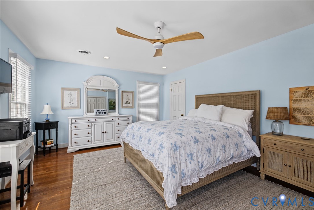Spacious room featuring hardwood flooring, multi-pane windows with integrated blinds, and a contemporary ceiling fan with wood-finish blades
