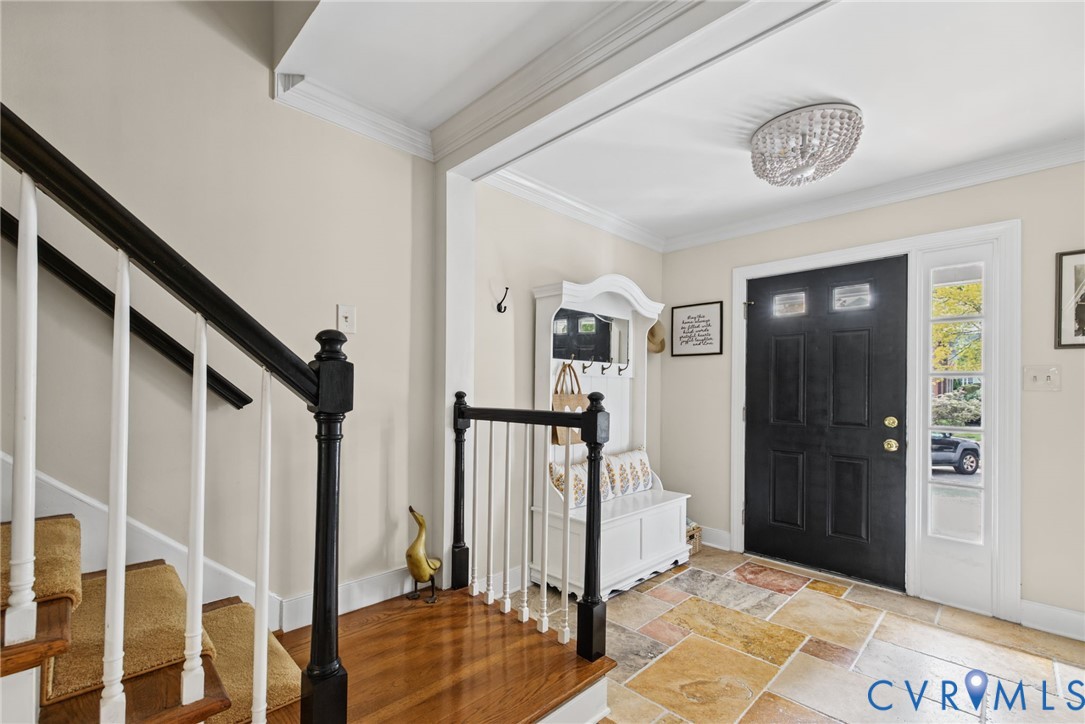 Foyer featuring natural stone flooring, a dark-finished wooden staircase with white balusters, crown molding, and a beaded semi-flush mount light fixture Foyer featuring natural stone flooring, a dark-finished wooden staircase with white balusters, crown molding, and a beaded semi-flush mount light fixture