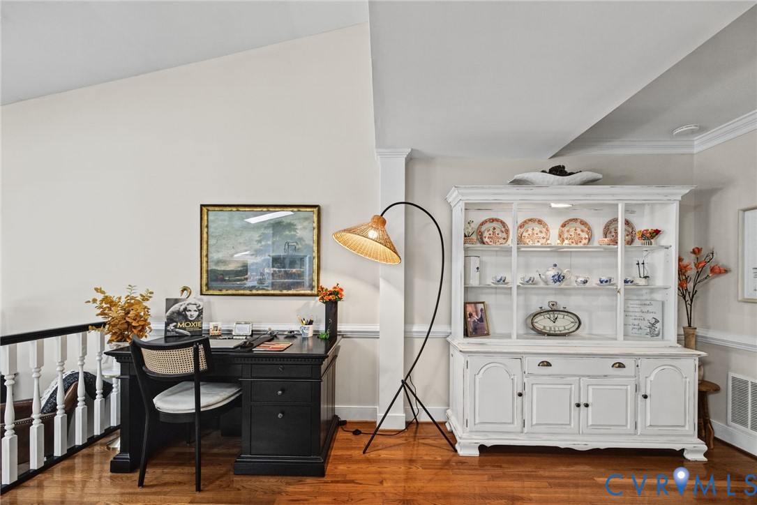 Vaulted ceiling with crown molding, wood-finish flooring, and white spindle railing