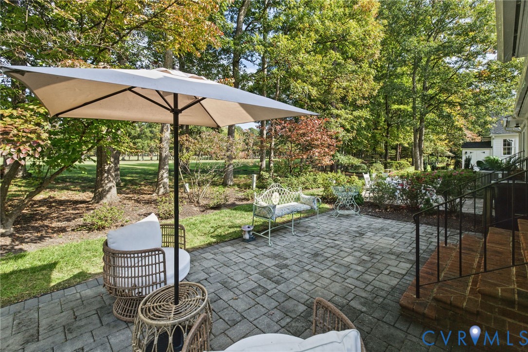 Paver stone patio featuring brick steps, metal railing, and mature landscaping