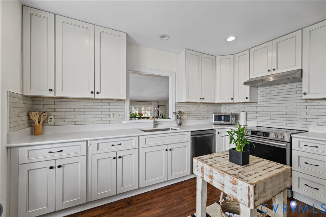 Kitchen featuring white cabinetry, solid surface countertops, subway tile backsplash, stainless steel appliances, and wood-finish flooring Kitchen featuring white cabinetry, solid surface countertops, subway tile backsplash, stainless steel appliances, and wood-finish flooring