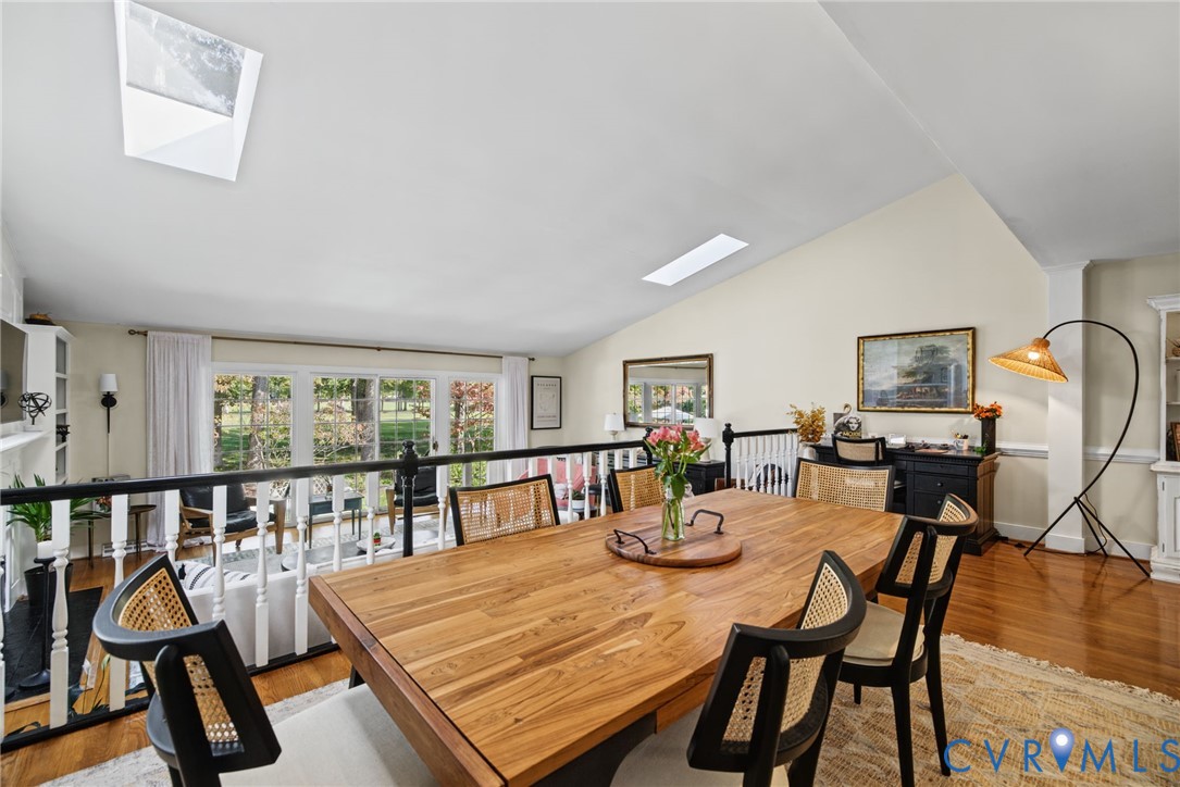 Vaulted ceilings featuring dual skylights, wood-finish flooring, and a decorative black spindle railing