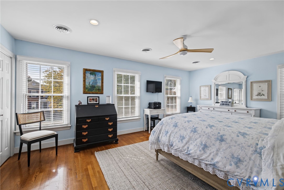 Spacious room featuring wood-finish flooring, recessed lighting, a modern ceiling fan, and multiple windows with horizontal blinds