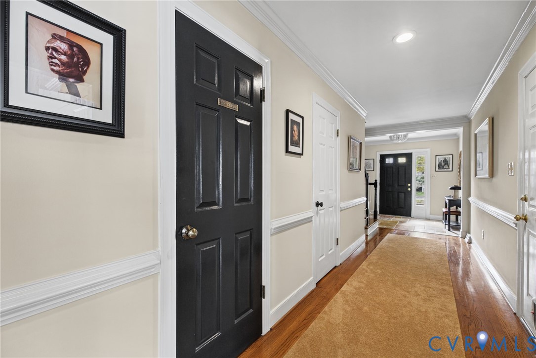 Interior hallway featuring wood-finish flooring, crisp crown molding, chair rail trim, recessed lighting, and solid-core panel doors Interior hallway featuring wood-finish flooring, crisp crown molding, chair rail trim, recessed lighting, and solid-core panel doors
