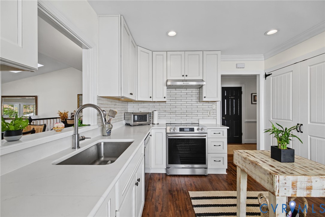 Kitchen featuring white cabinetry, light-toned stone-finish countertops, stainless steel appliances, subway tile backsplash, and wood-finish flooring Kitchen featuring white cabinetry, light-toned stone-finish countertops, stainless steel appliances, subway tile backsplash, and wood-finish flooring