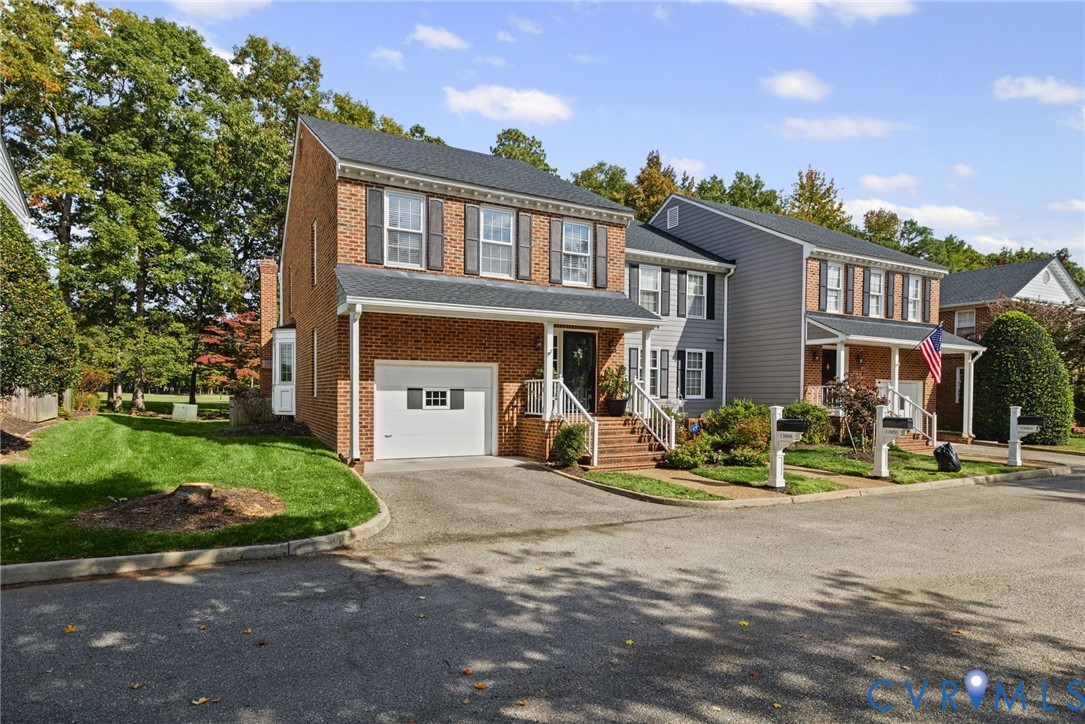 Two-story colonial exterior featuring a brick facade, asphalt shingle roof, attached single-car garage, covered front porch with railings, and multi-pane windows with shutters Two-story colonial exterior featuring a brick facade, asphalt shingle roof, attached single-car garage, covered front porch with railings, and multi-pane windows with shutters