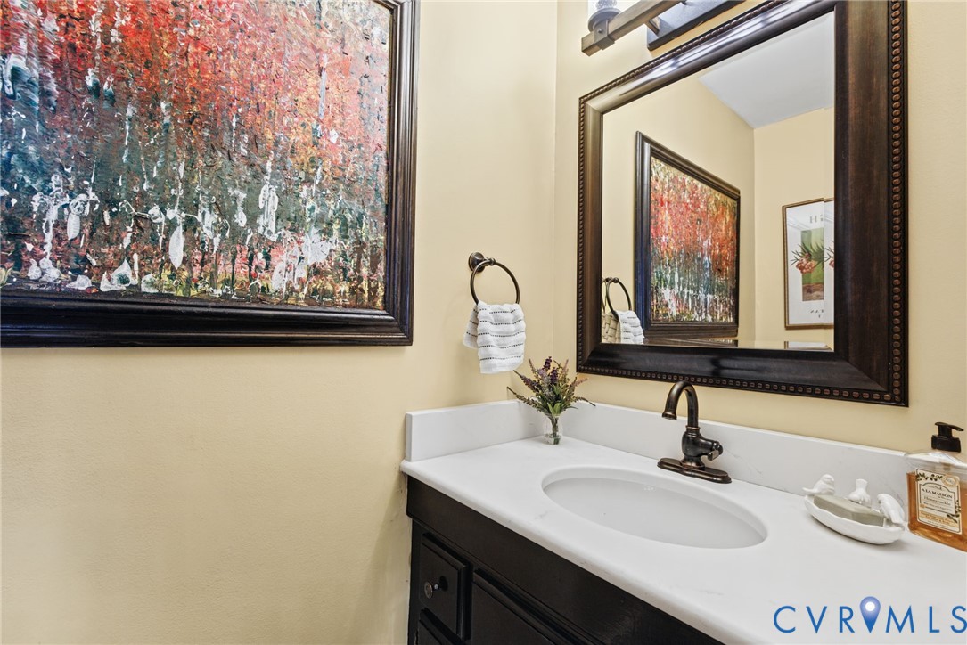 Vanity featuring dark-finish cabinetry, a white stone-surface countertop, an undermount oval sink, an oil-rubbed bronze faucet, and a coordinating framed mirror Vanity featuring dark-finish cabinetry, a white stone-surface countertop, an undermount oval sink, an oil-rubbed bronze faucet, and a coordinating framed mirror