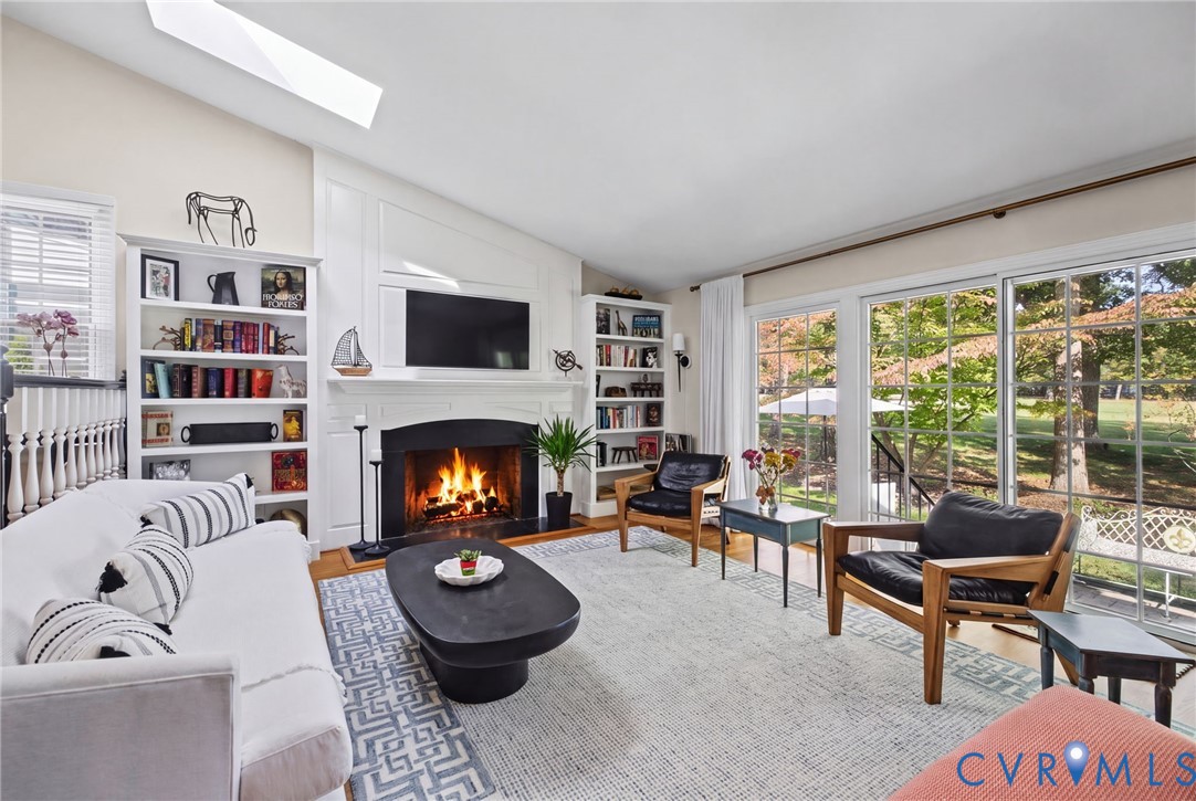 Vaulted ceiling with a skylight, fireplace featuring a classic mantel, built-in shelving, and large sliding glass doors