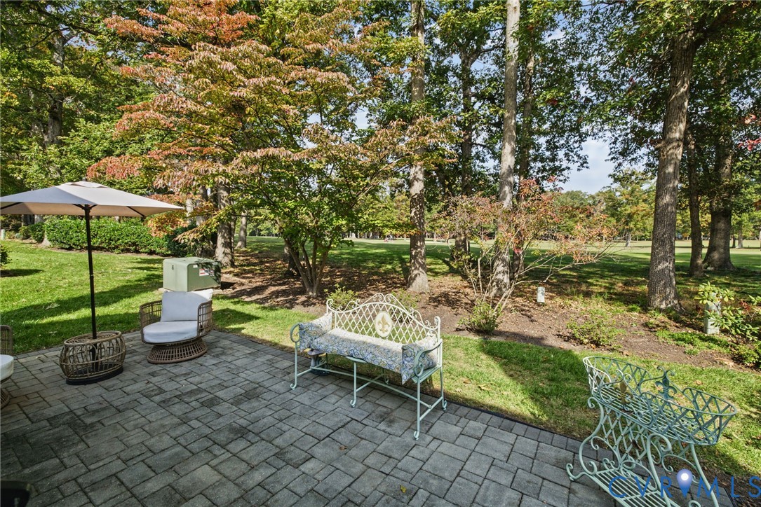 Paver patio featuring a grey rectangular stone pattern, surrounded by a landscaped lawn and mature tree canopy with golf course views