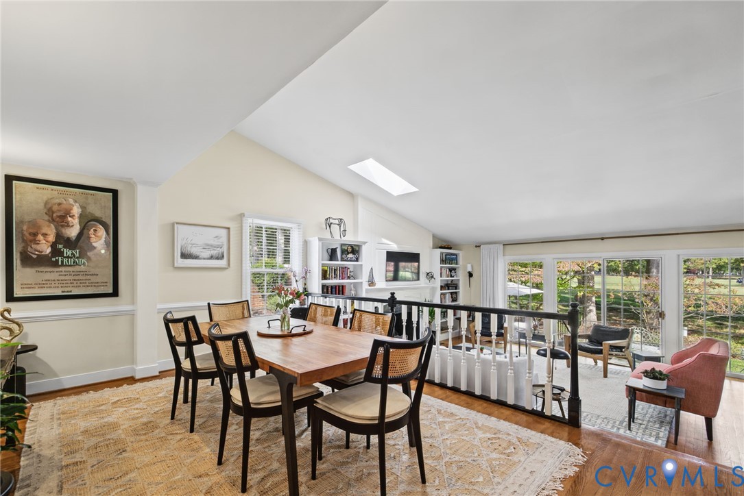 Vaulted ceiling with integrated skylight, hardwood flooring, built-in shelving, and large sliding glass doors