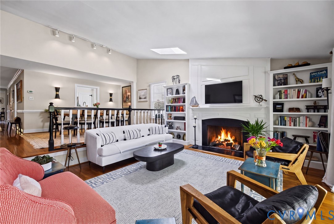 Living area featuring a fireplace with a white mantel, built-in shelving, wood-finish flooring, a skylight, and track lighting