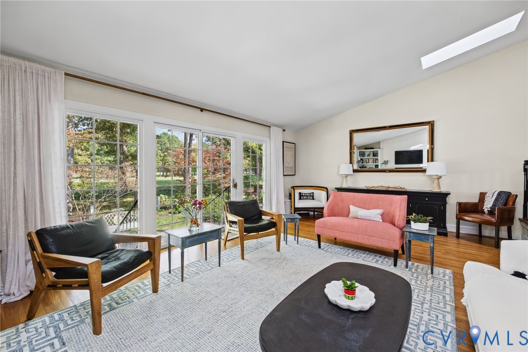 Vaulted ceilings with a recessed skylight, expansive floor-to-ceiling glass sliding doors, and wood-finish flooring