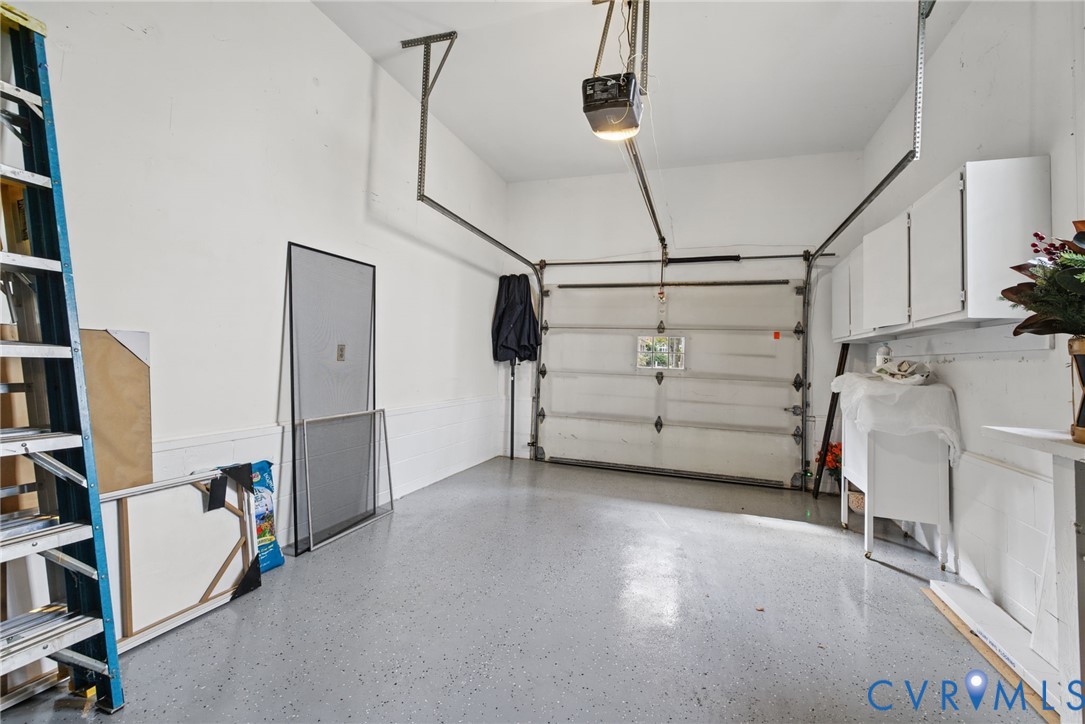 Attached garage featuring a durable epoxy concrete floor, white wall-mounted storage cabinetry, and an overhead door mechanism