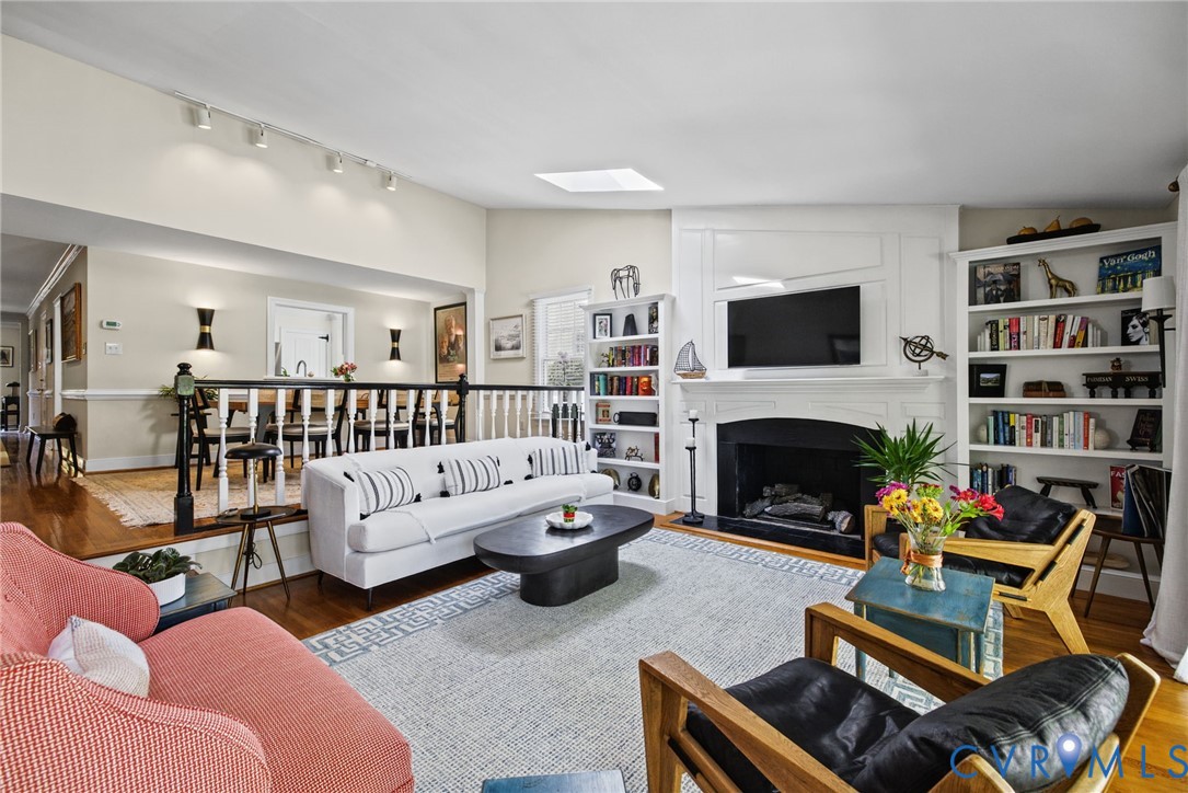 Living space featuring a central fireplace with decorative millwork, built-in floor-to-ceiling shelving, track lighting, skylight, and wood-finish flooring