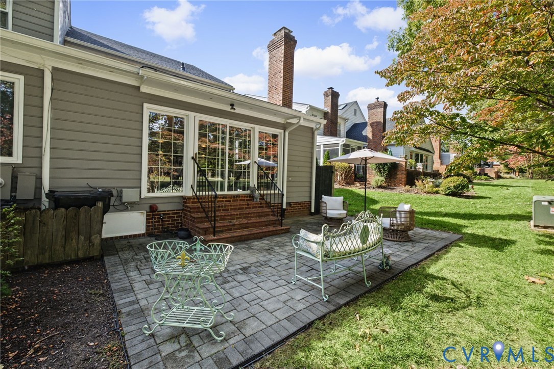 Rear exterior featuring lap siding, brick masonry chimney, paver patio, brick steps with iron railings, and sliding glass sliding doors
