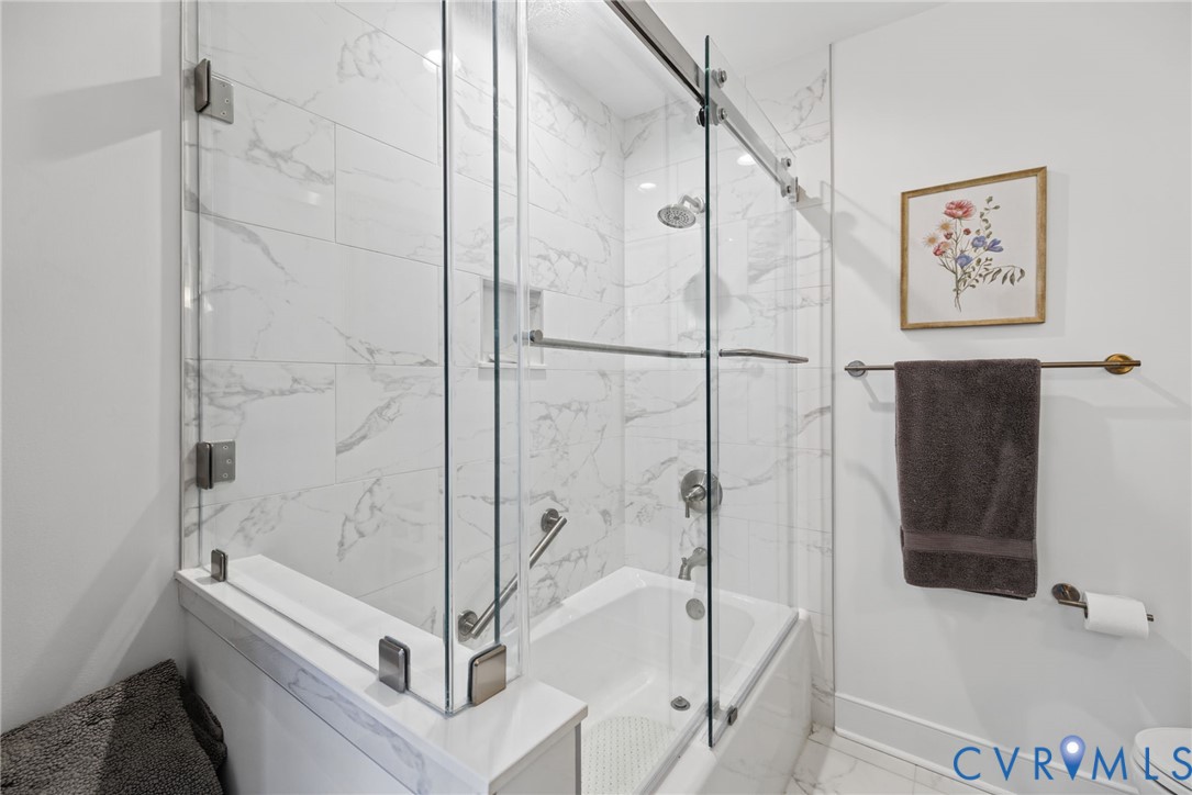 Frameless glass shower enclosure, tub with surround featuring rectified-edge tile, integrated wall niche, and metal hardware