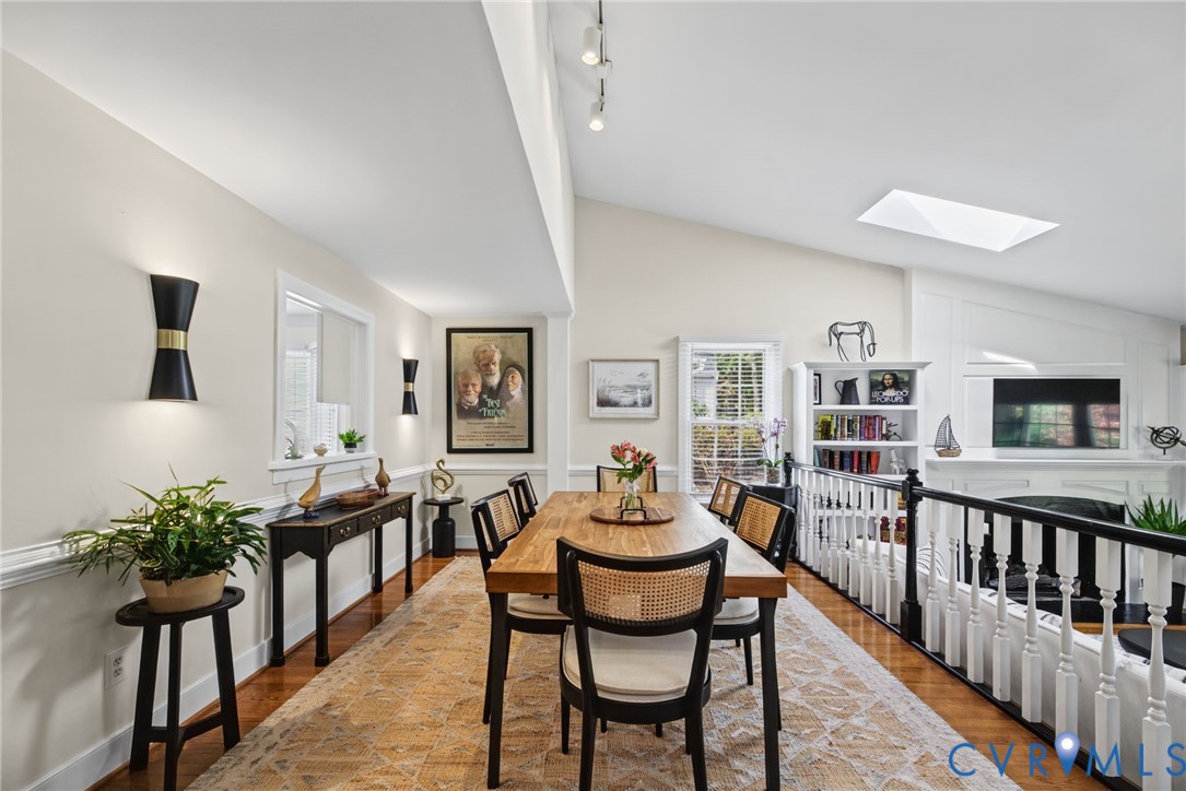 Vaulted ceiling with skylight, wood-finish flooring, built-in fireplace, and wall-mounted sconce lighting