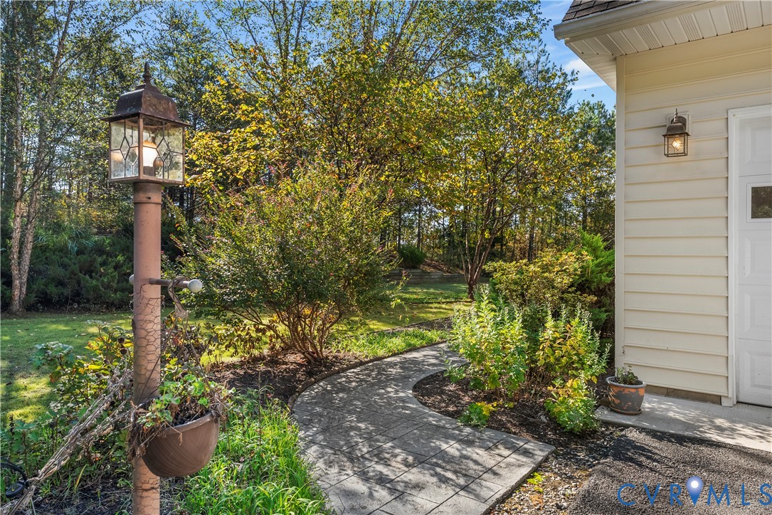 Landscaped exterior featuring light-colored horizontal siding, a stone paver walkway, mature trees, and a decorative metal post lamp