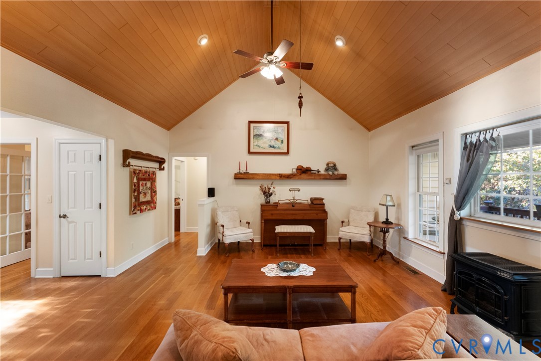 Vaulted tongue-and-groove wood ceiling, polished wood flooring, built-in wooden mantel, recessed lighting, and black wood-burning stove