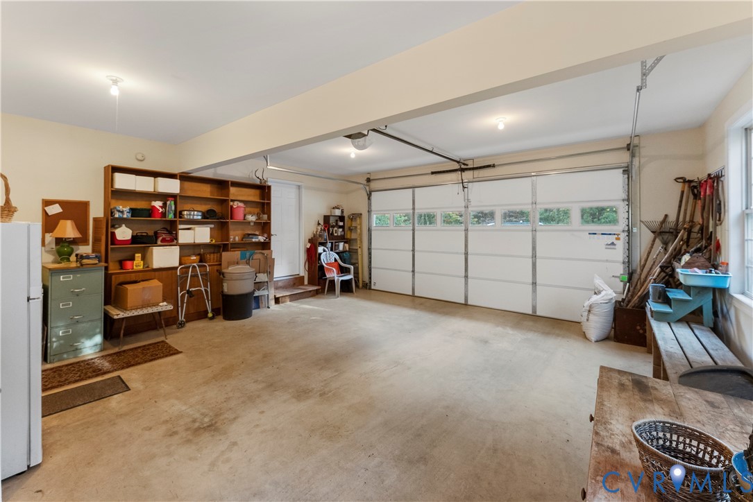 Attached two-car garage featuring a sectional garage door with windows, concrete flooring, built-in wooden shelving, and interior lighting