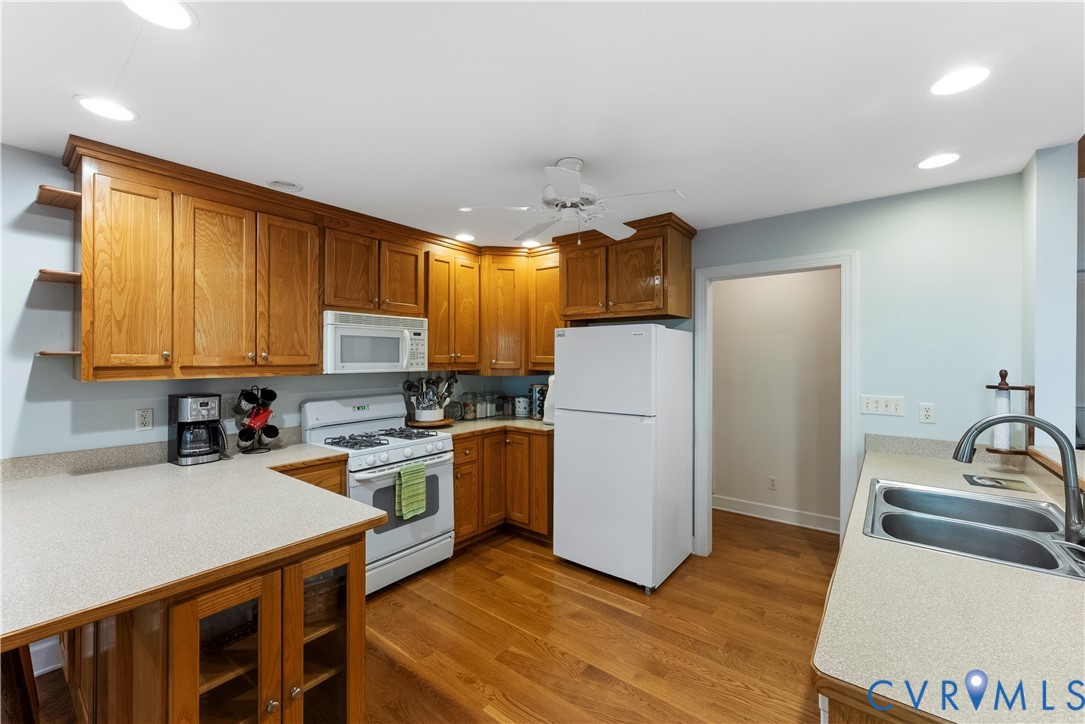 Kitchen featuring wood cabinetry, laminate countertops, wood-finish flooring, a white gas range with an integrated microwave, and a double-basin stainless steel sink