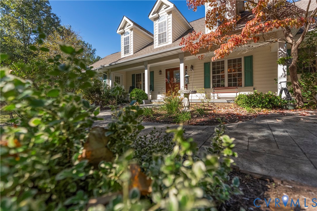 Cape Cod style exterior featuring horizontal lap siding, dormer windows with muntin-grille detailing, a covered front porch, and a stone-patterned paver walkway