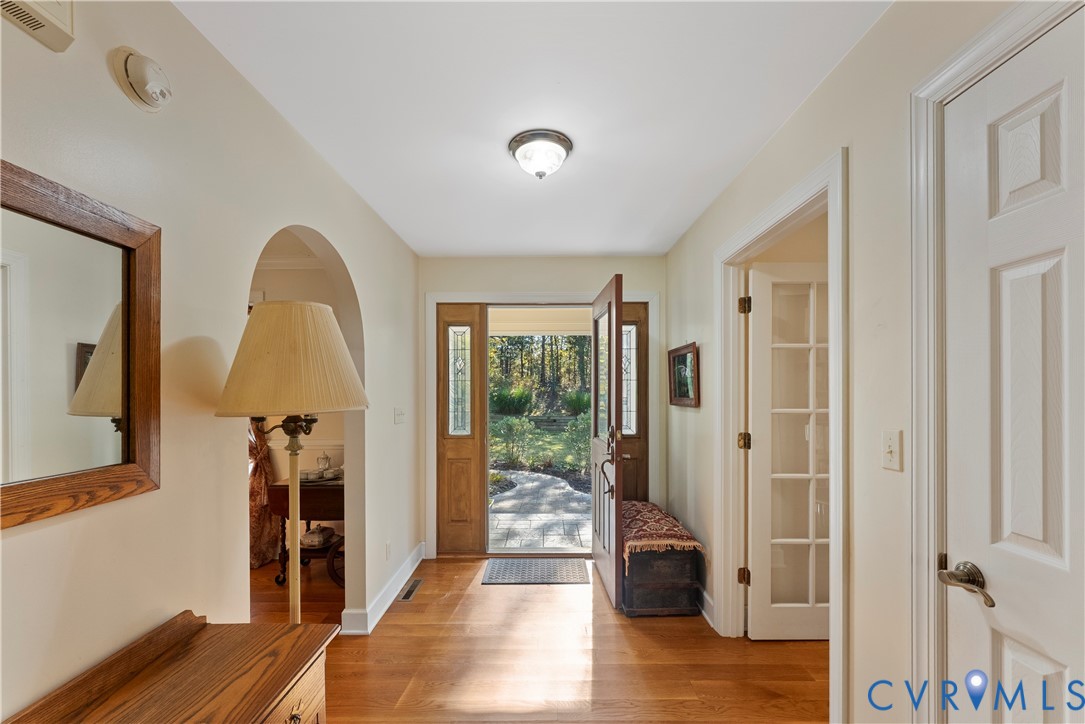 Foyer featuring wood-finish flooring, an arched architectural opening, and a natural wood-finish front door with glass sidelights